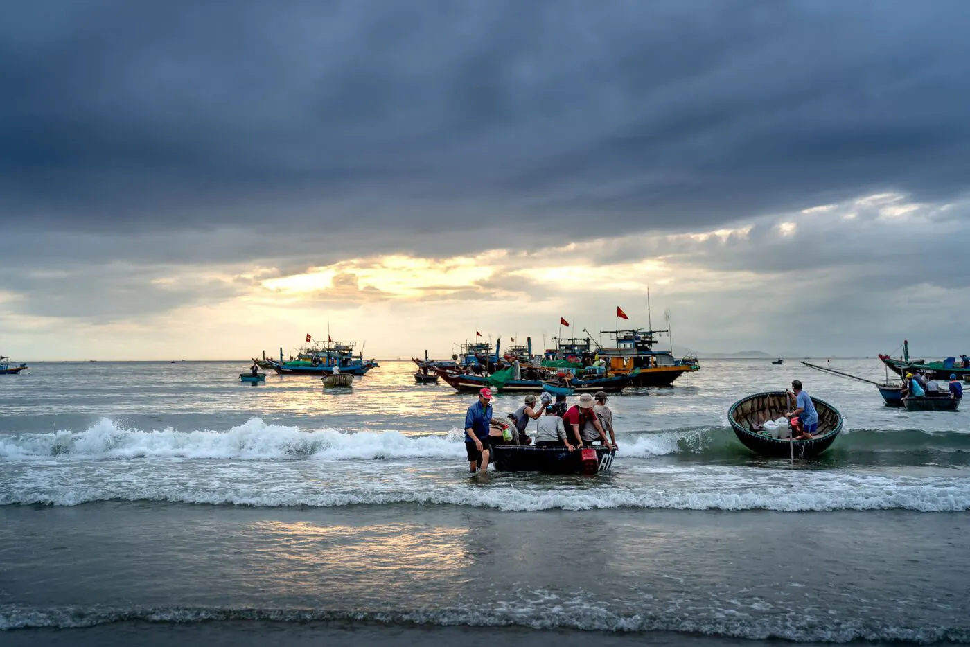 Dawn at My Khe Beach, Da Nang: swimmers and a round bamboo basket boat in the surf, construction cranes on the skyline behind.
