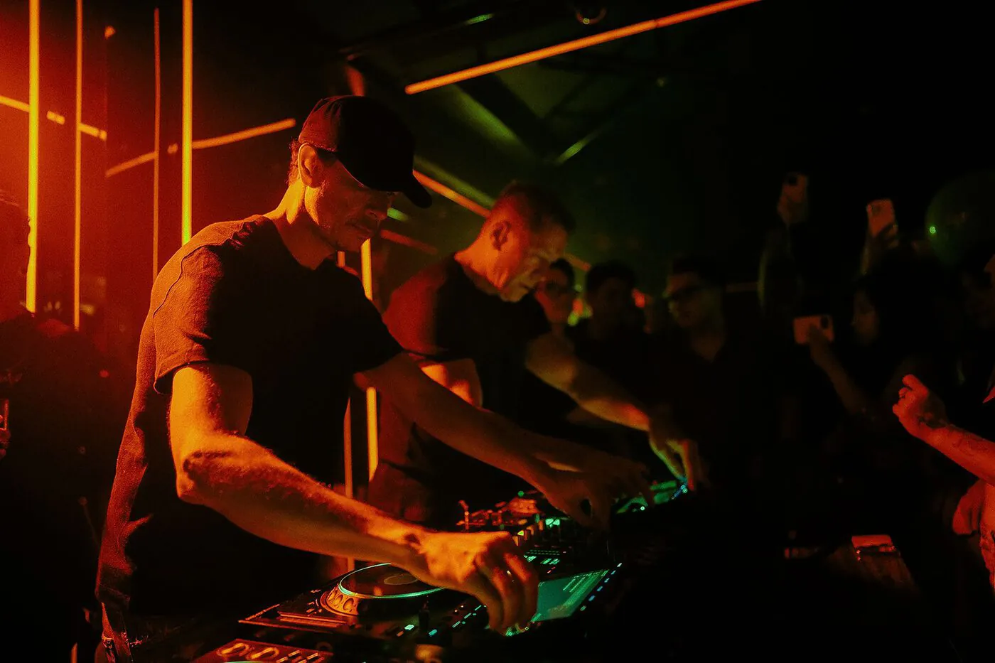A DJ at the booth under red light with the crowd close.